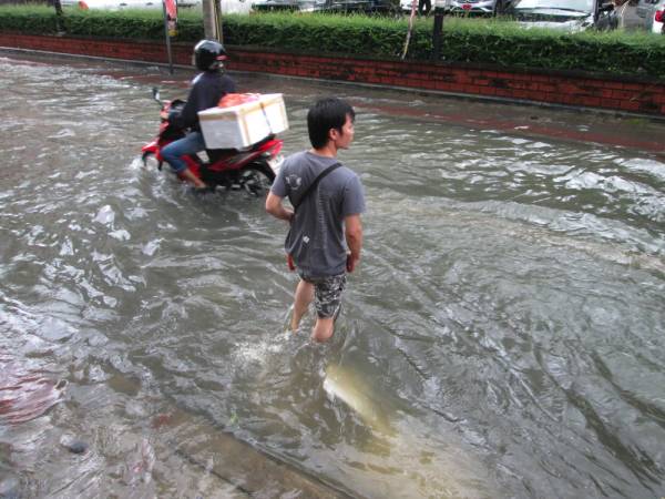 膝まで水が及んでいながらも道路を渡る現地人